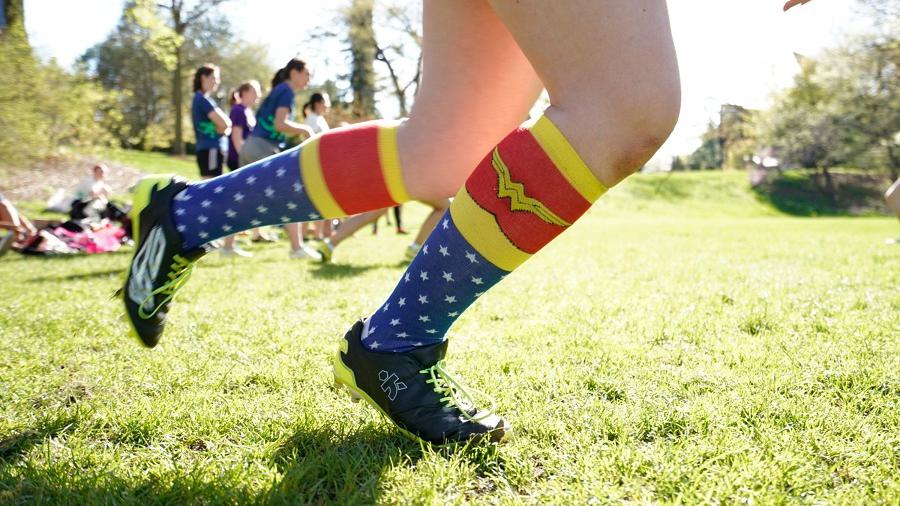 A Wellesley College student with cleats and Wonder Woman stockings on runs across a green playing field