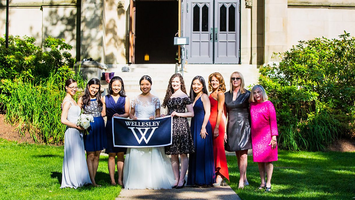 Nine women pose for a photo with the bride in the center holding a Wellesley banner.
