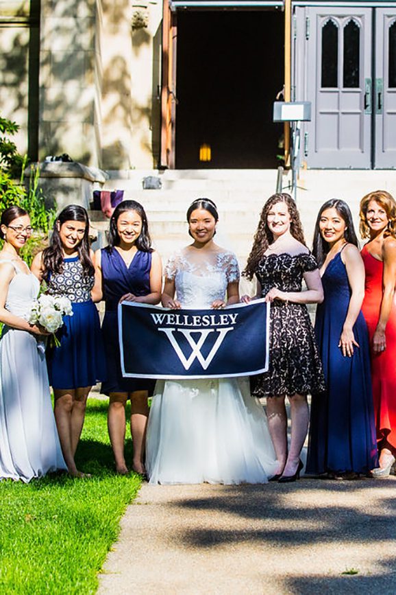 Nine women pose for a photo with the bride in the center holding a Wellesley banner.