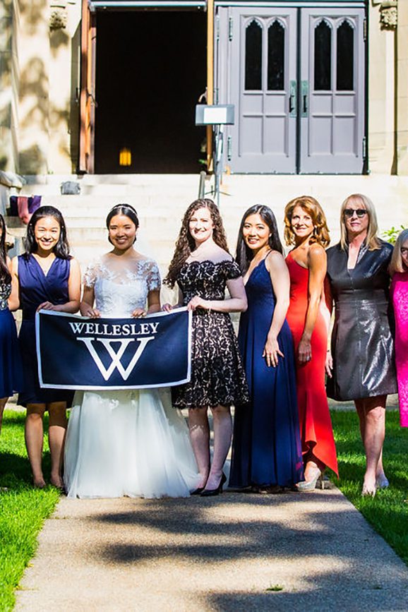 Nine women pose for a photo with the bride in the center holding a Wellesley banner.