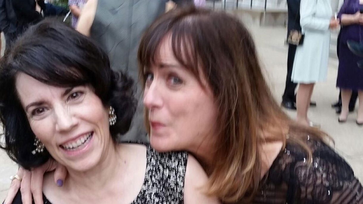 A woman leans over and pretends to kiss her friend who is leaning away from her and smiling.