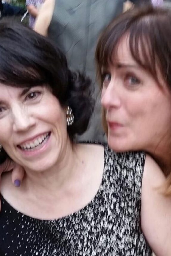 A woman leans over and pretends to kiss her friend who is leaning away from her and smiling.