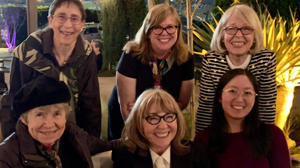Six women gather for a group photo and all smile at the camera