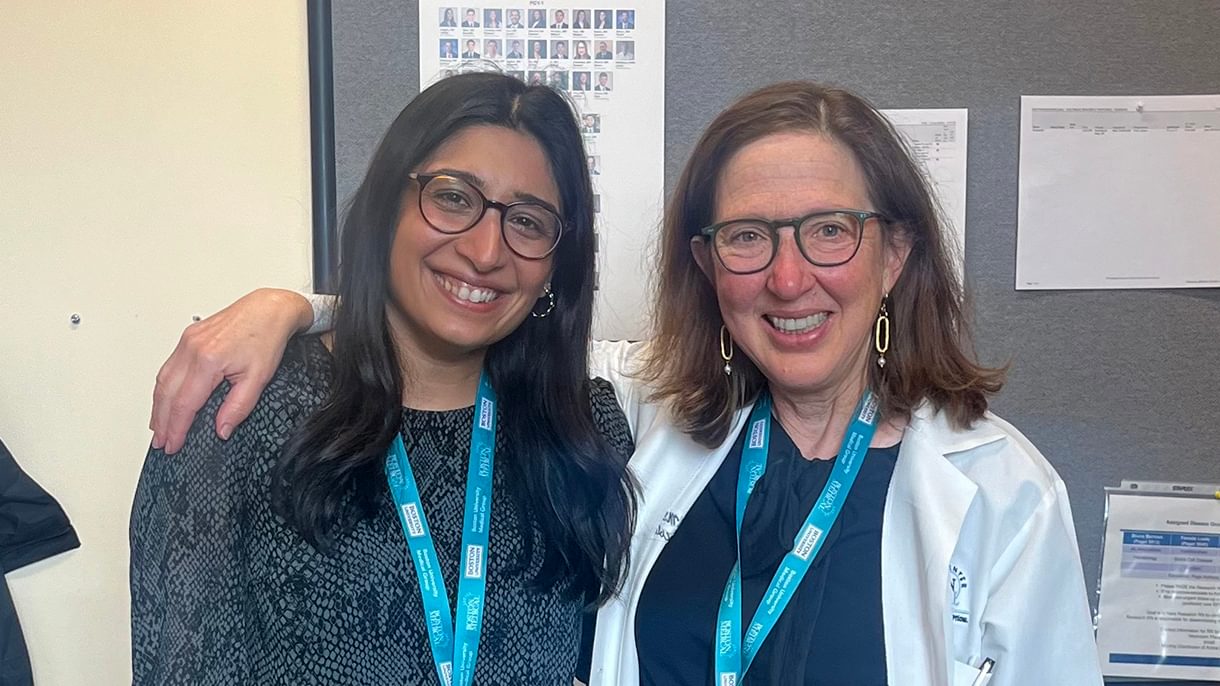 Two women pose for a photo and smile. One woman drapes her arm around the other.