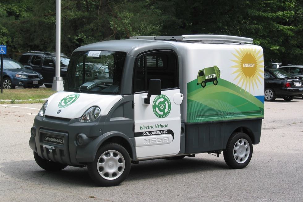 An electric vehicle with a green Wellesley logo and clip art of a sun with the word "energy" and a truck with the word "waste."