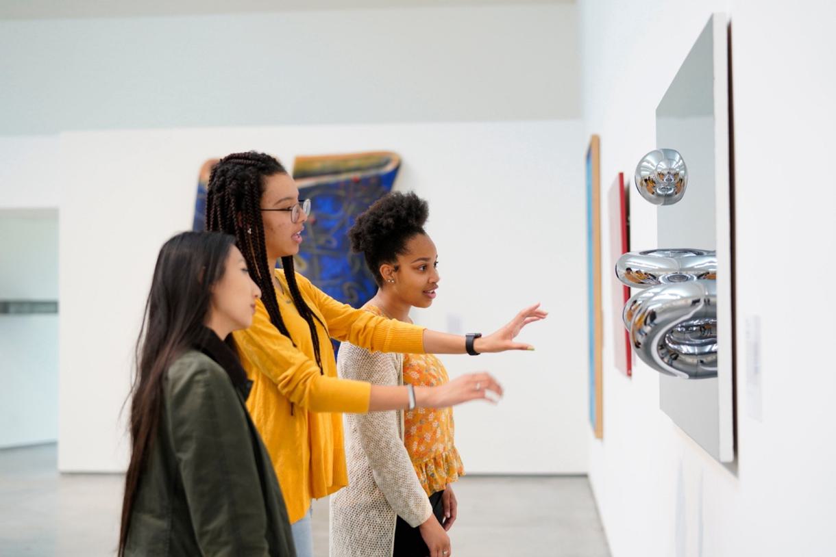 3 students stand in front of a metal sculpture art piece.