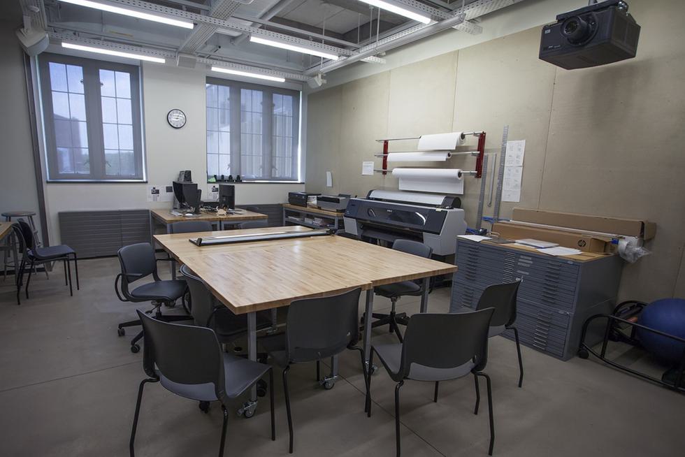 An empty media room. There is a table in the center with seven gray chairs.