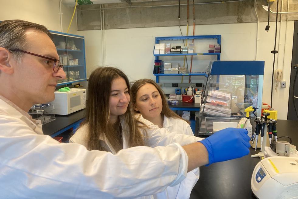 Two students watch their professor demonstrate titration.