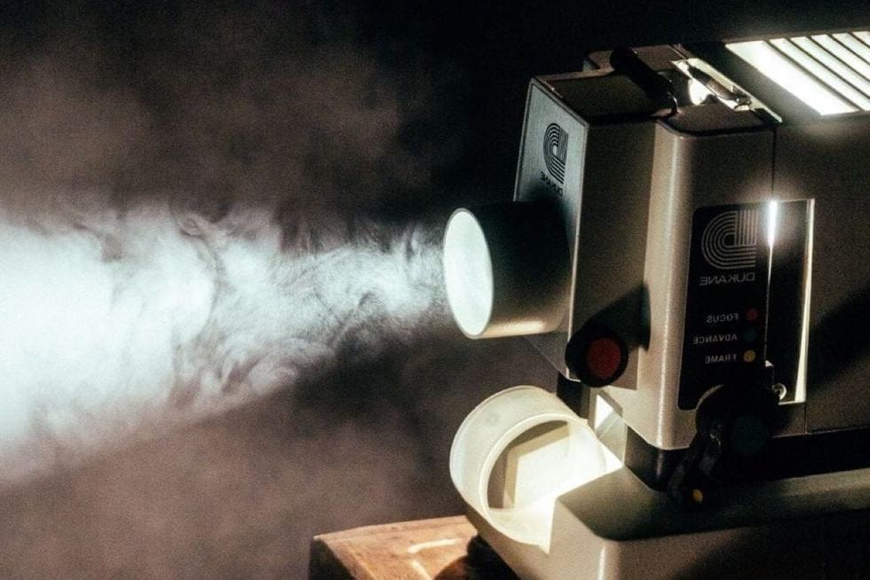 A projector projecting a bright image, illuminating particles in the dusty or smokey air.