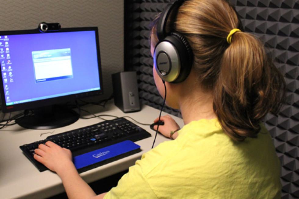 A student wearing headphones uses a desktop computer.