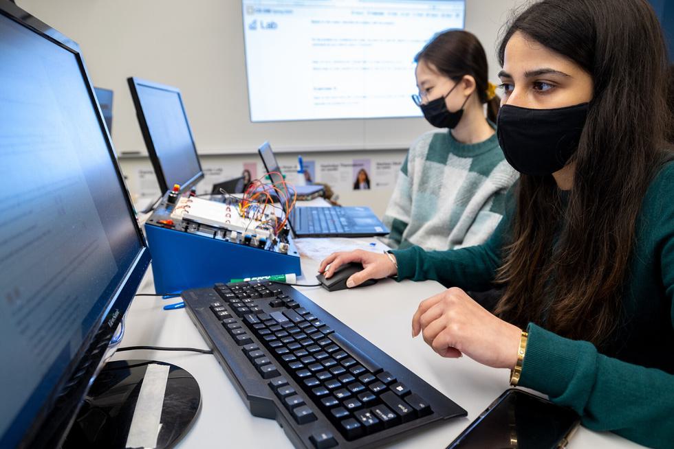 Two students wearing mask work at computers.