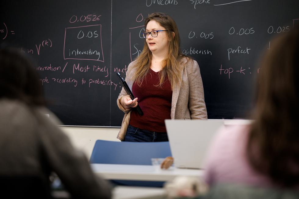 Carolyn Anderson stands in front of a chalkboard and lectures to a class. She is holding an iPad.