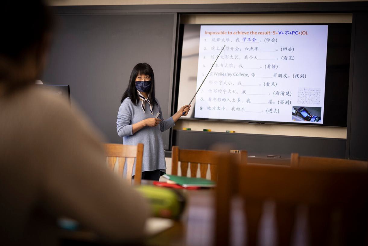 An instructor points to Chinese sentences on a projected board in class.