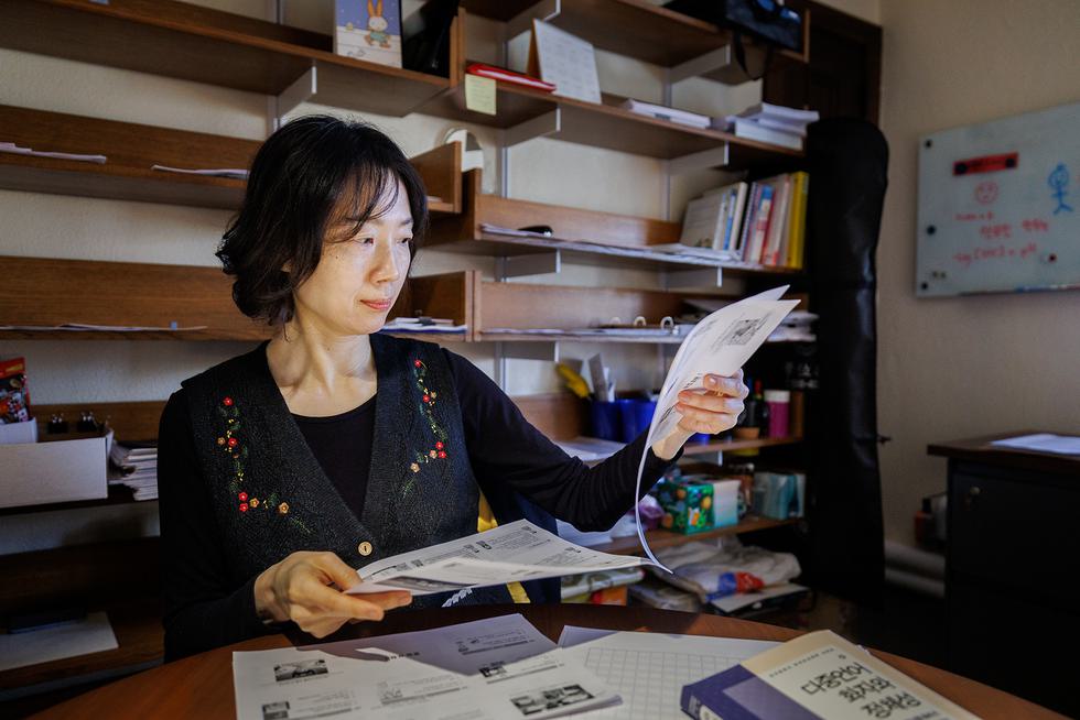 Professor Eun Ha Hwang sits at a table and examines papers, with wooden shelves seen behind her.