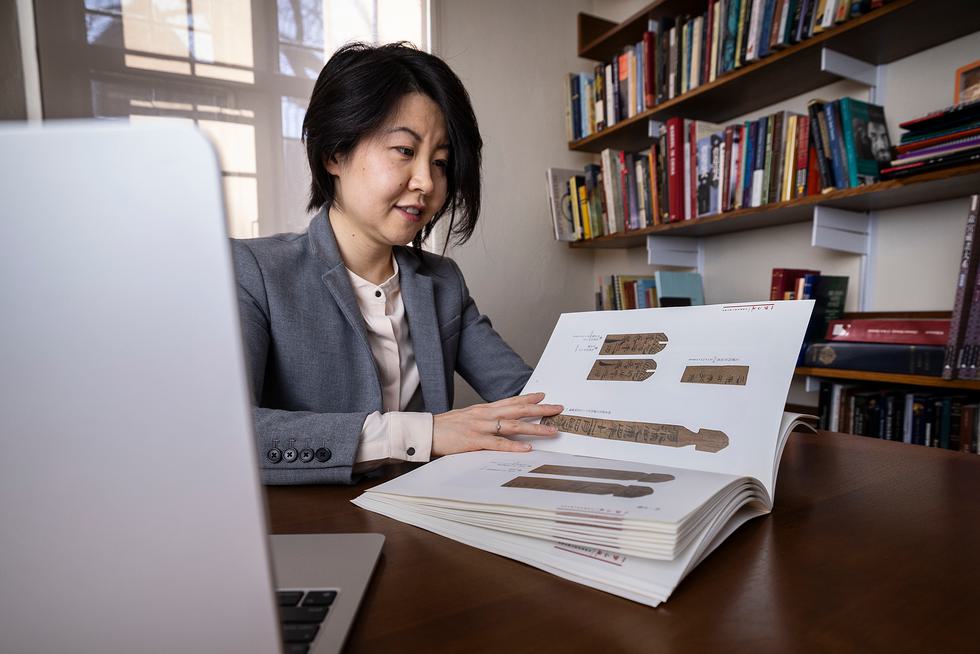Heng Du sits at her desk and flips through a book of early Chinese writing.