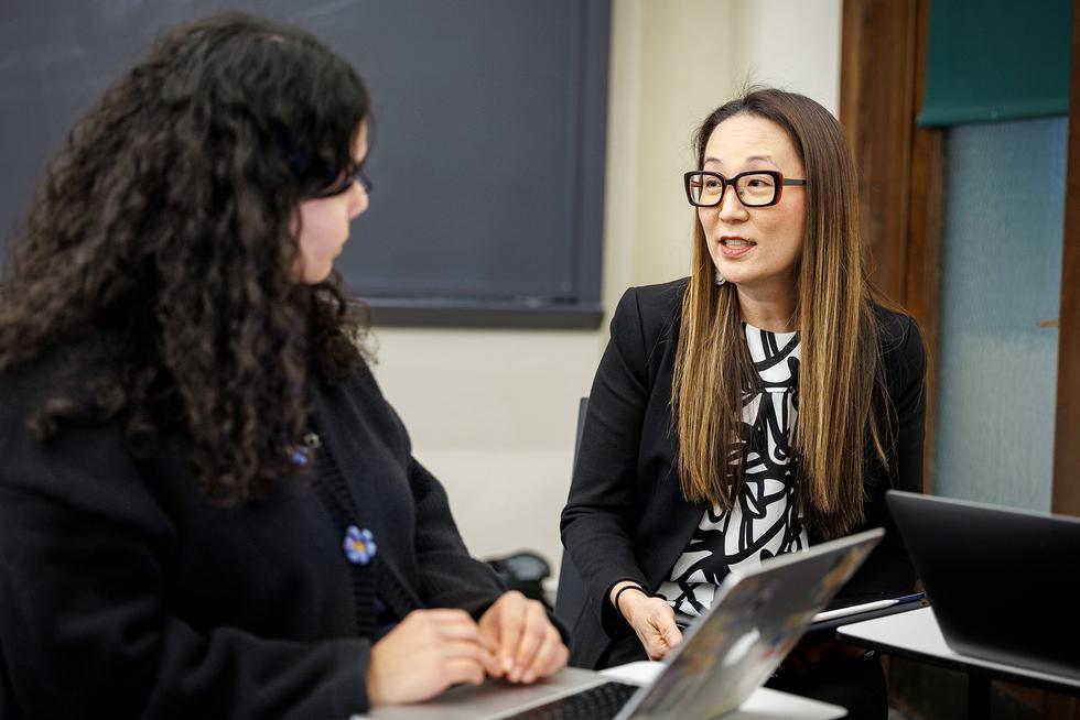 Professor Soo Hong sits and speaks with a student in a classroom.