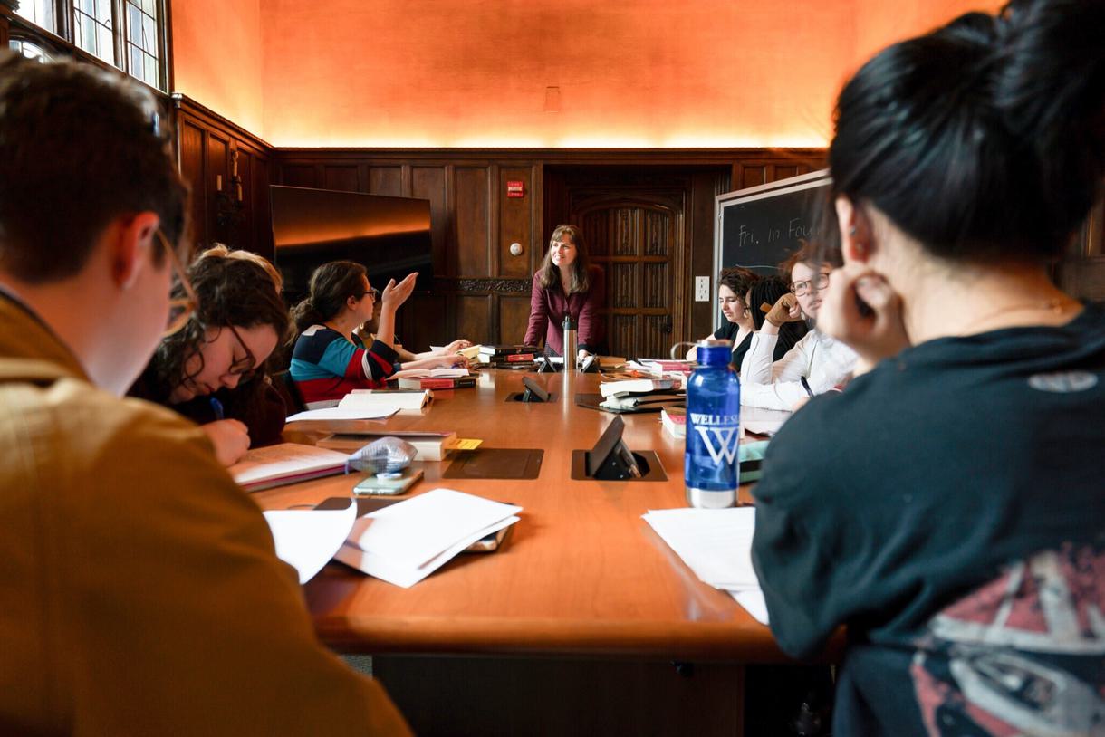 Students in class discuss with their professor around a table.