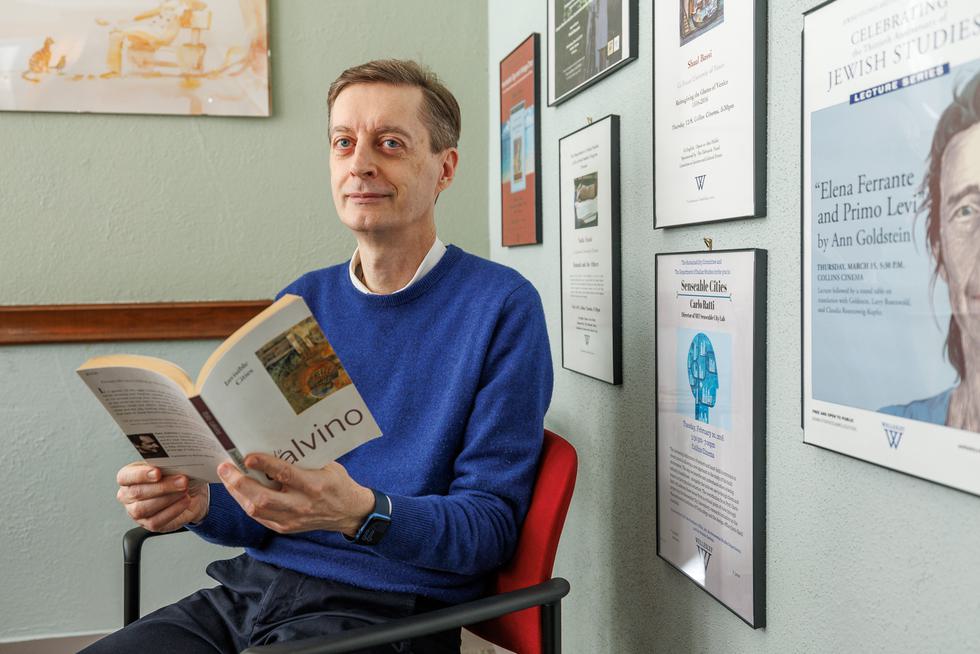 Sergio Parussa sits at a chair in his office reading a book. He is wearing a blue sweater and has a content, calm face.