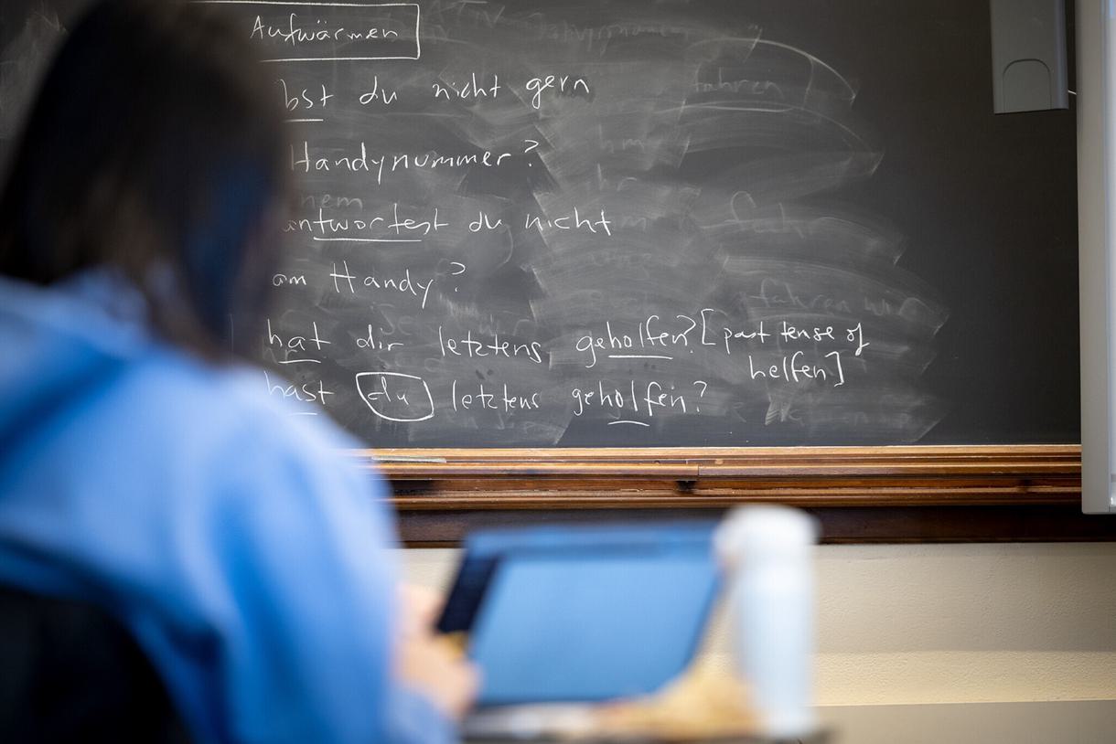 A student takes notes on their laptop in front of a chalkboard in German class.