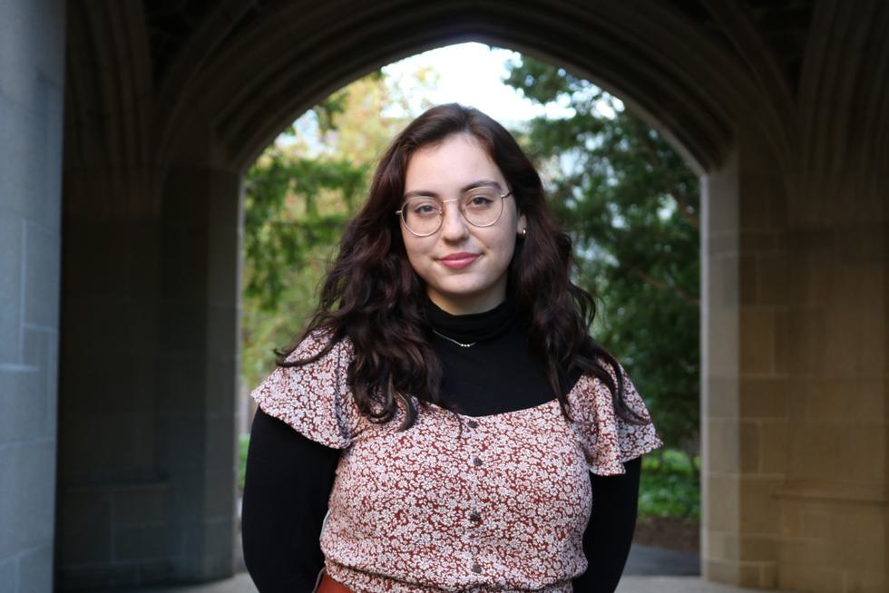 Jacq Roderick '23 softly smiles in front of an arch on Wellesley's campus.