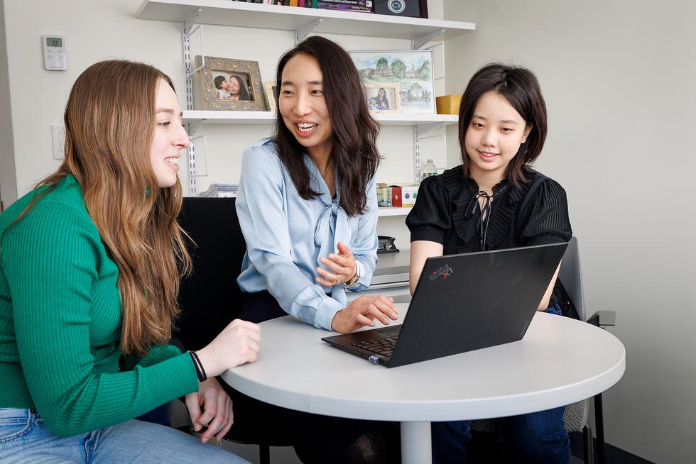 Three students smiling and talking while reading off of a laptop.
