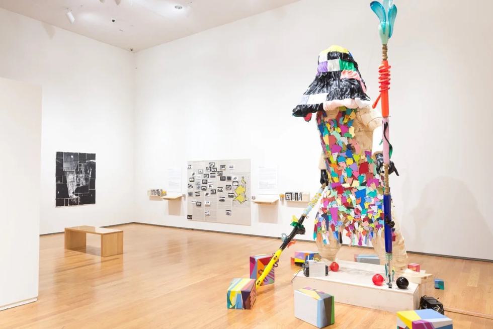 Colorful robot sculpture made from wood, glass, steel, and enamel stands tall in a gallery.