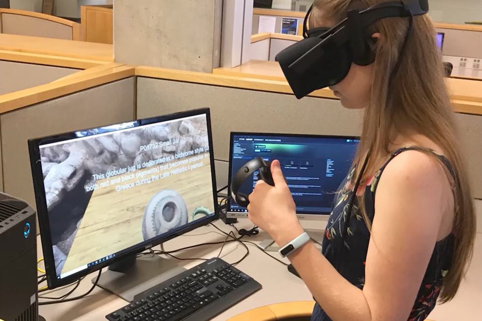 Student wears a VR headset while a screen mirrors what's on the display: a small globular jug from Greece's late Helladic period.