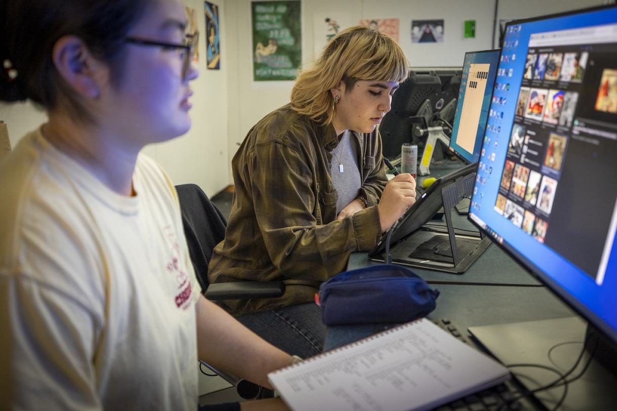 Student draws on a Wacom tablet while another reviews images on a screen.