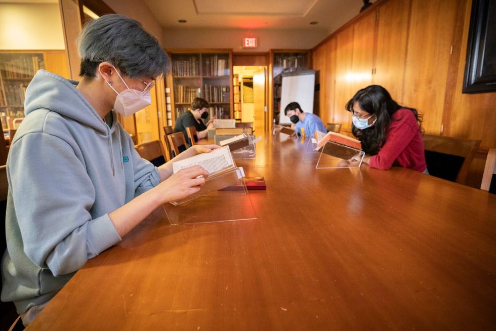 Students line a table examining old books from special collections.