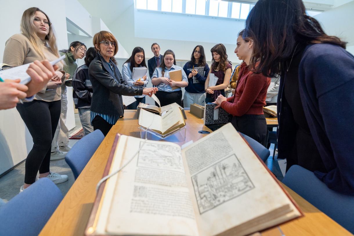 Students and professors gather around a table with old texts displayed on lucite bookstands.