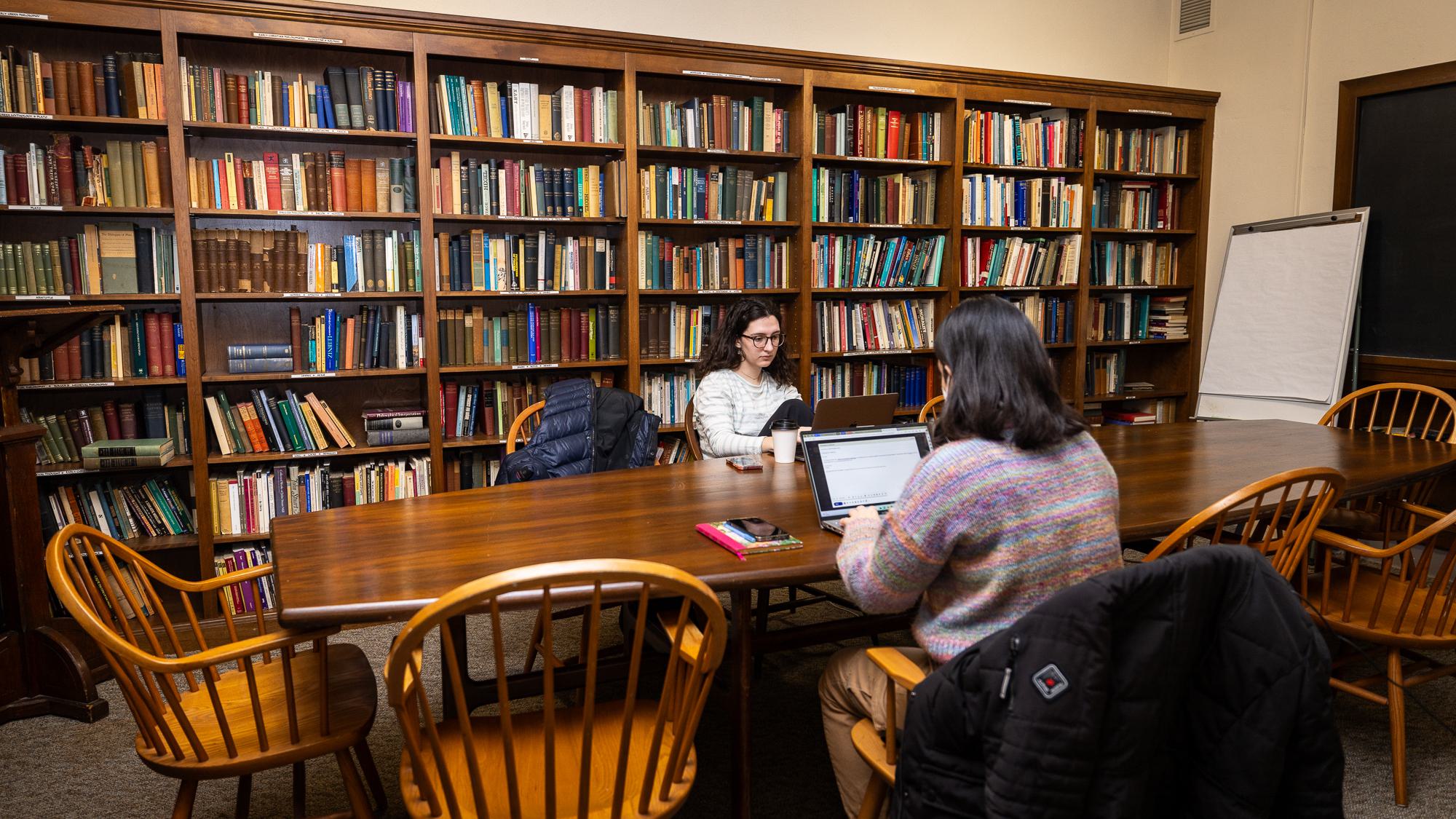 Students seated at table with bookshelves in background