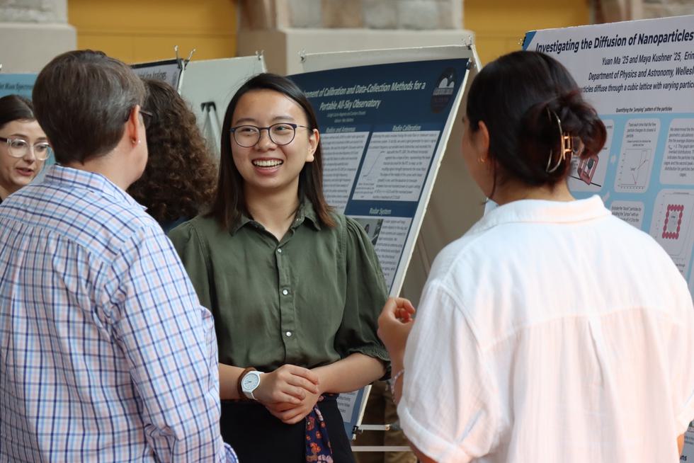 Students explain their poster to professor Katie Hall at a poster session.