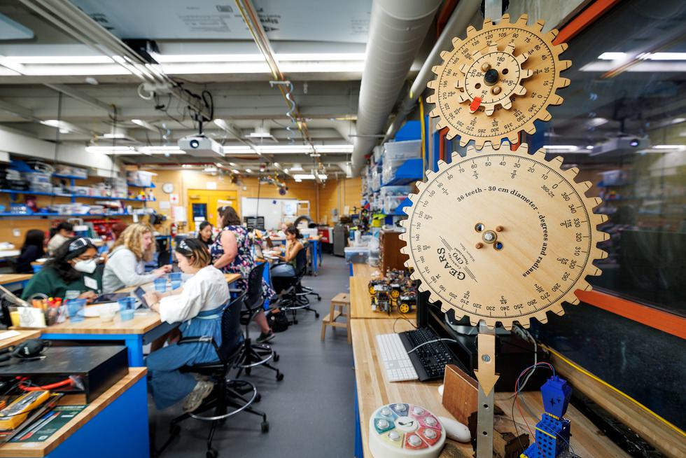 Students working at benches in the We-Lab with wooden gears in the foreground.