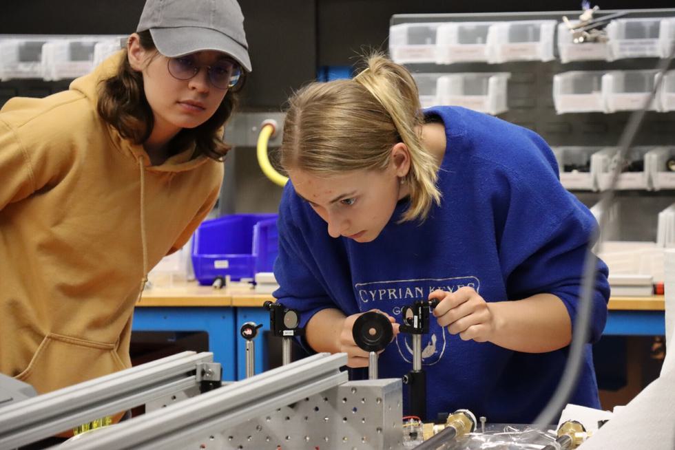 Students Alayna Shneider and Cora Barrett work on lasers in a physics laboratory room.
