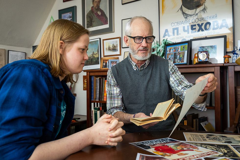 Thomas Hodge shows a student a book and a piece of paper. They are both sitting at a table.