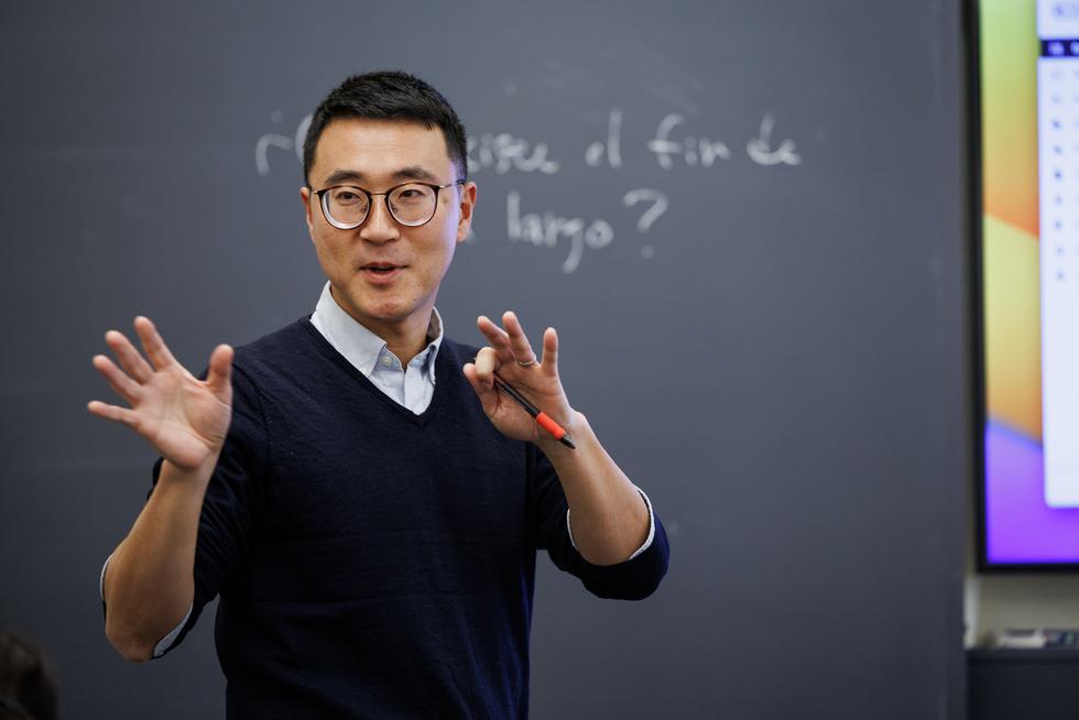 Koichi Hagimoto stands in front of a chalkboard and lectures to a class.