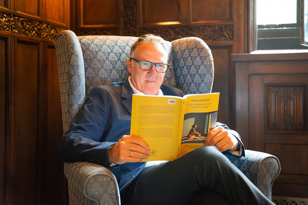 Carlos Ramos, seated in a wing chair, reading his book