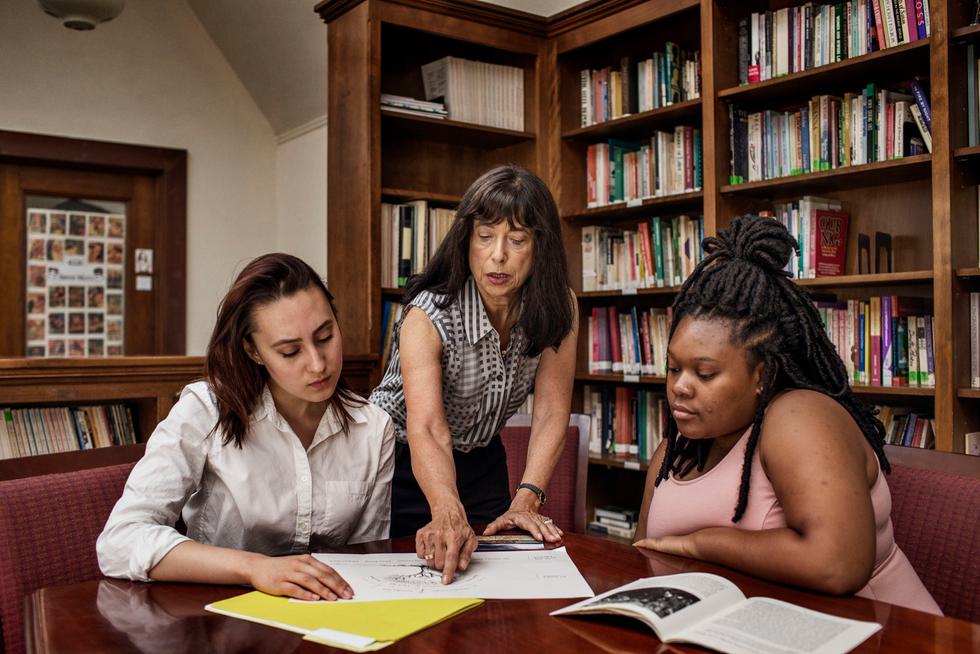 Professor Hertz points out parts of a diagram on a table to two students sitting around her.