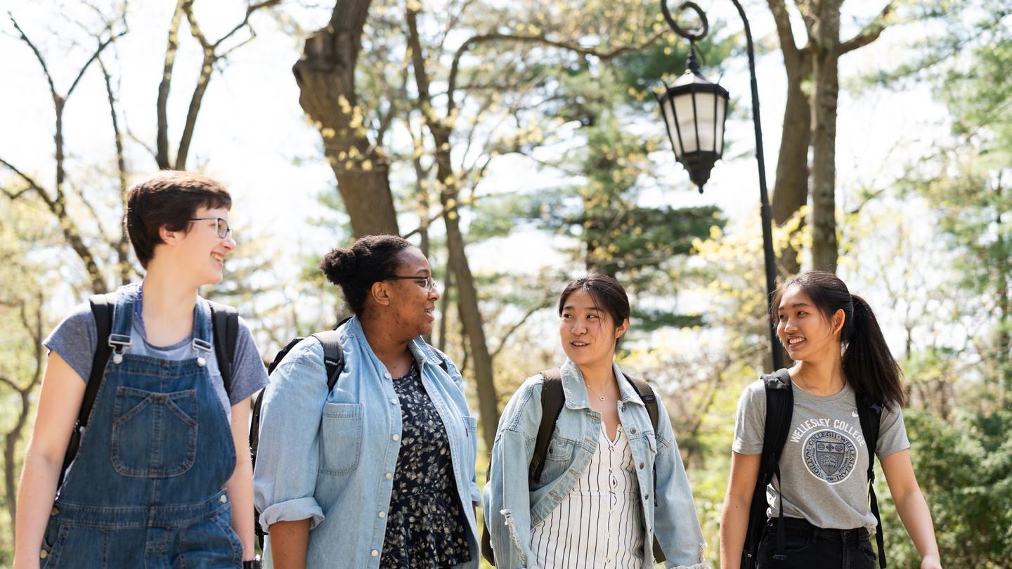 Four students chat while walking outside on a sunny spring day.