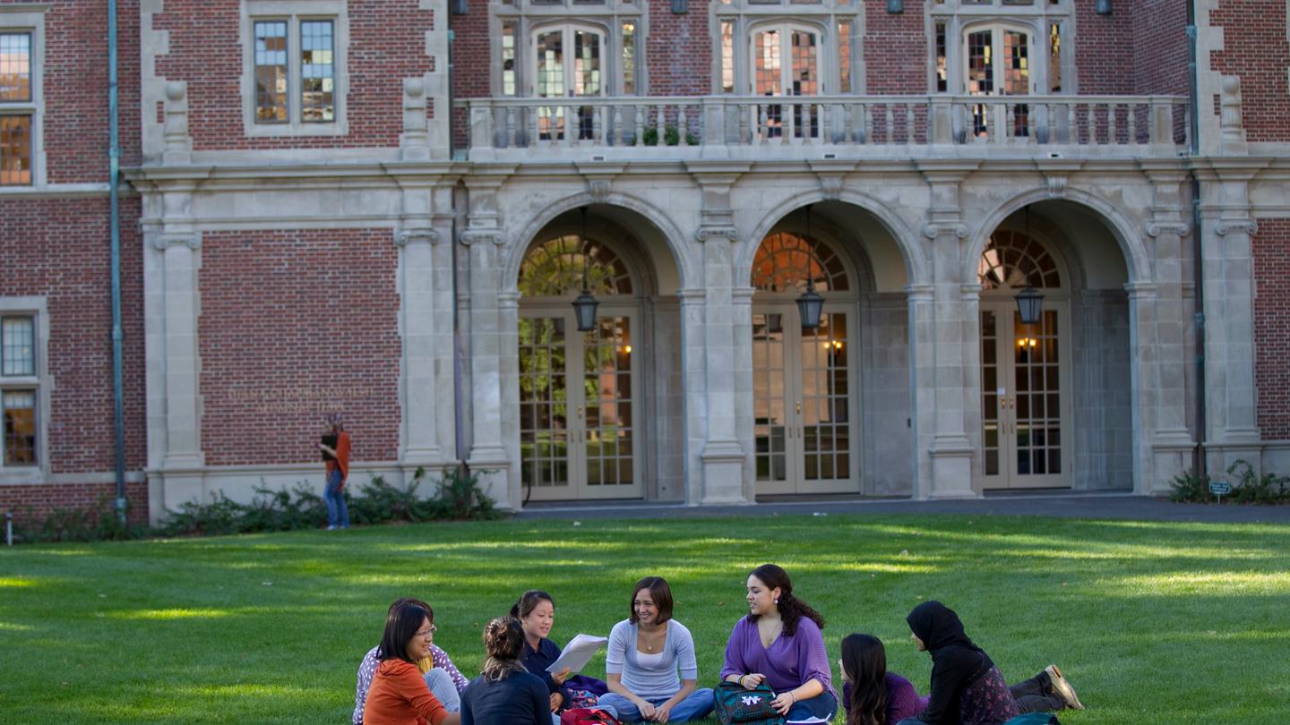 A group of students sit on the lawn outside Alumnae Hall.