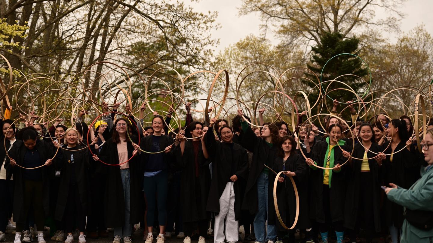 Group of students standing outside smiling and holding hoops above their heads.