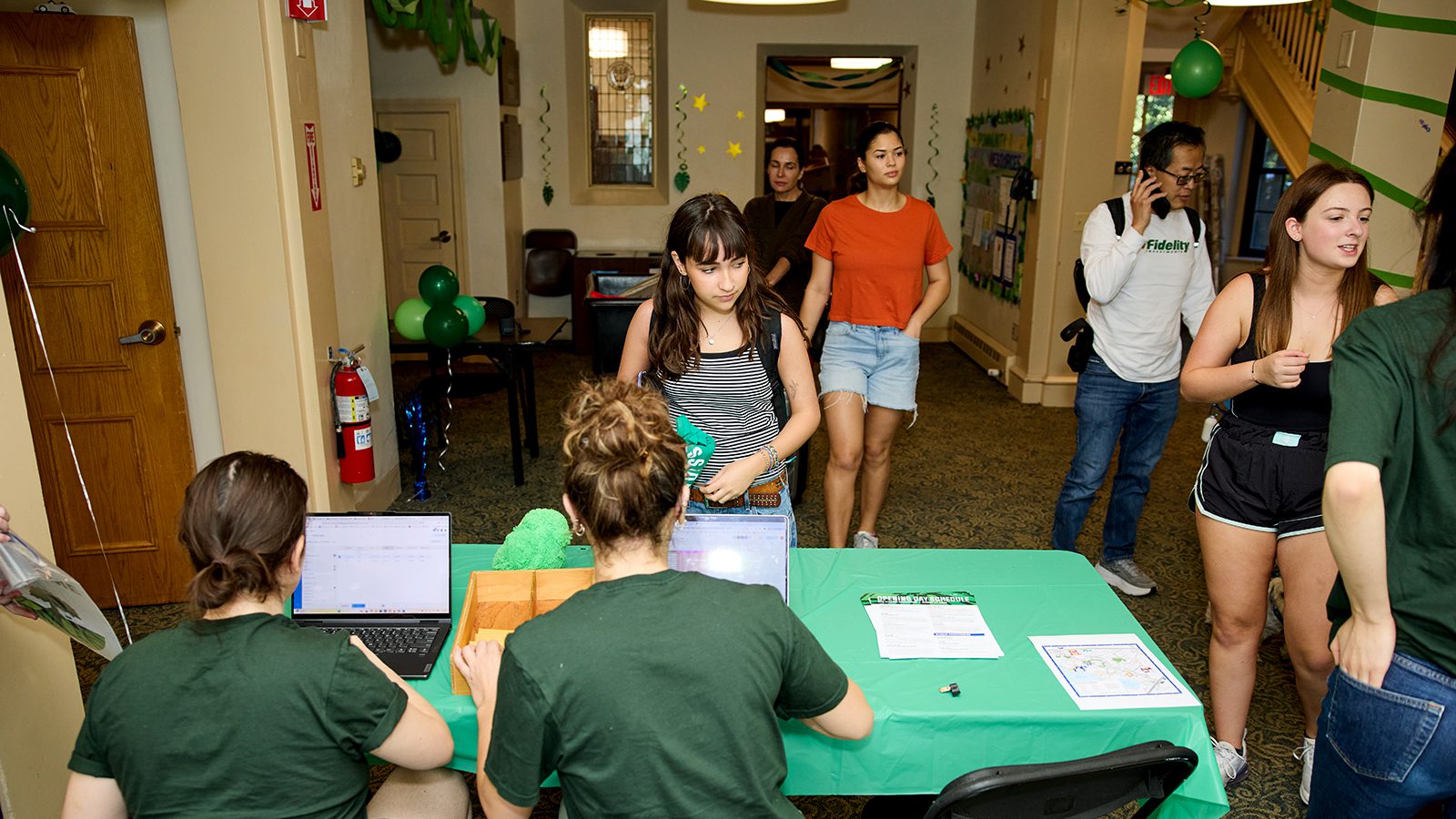 A student stands facing a table where two Wellesley students sit. Others walk past them.