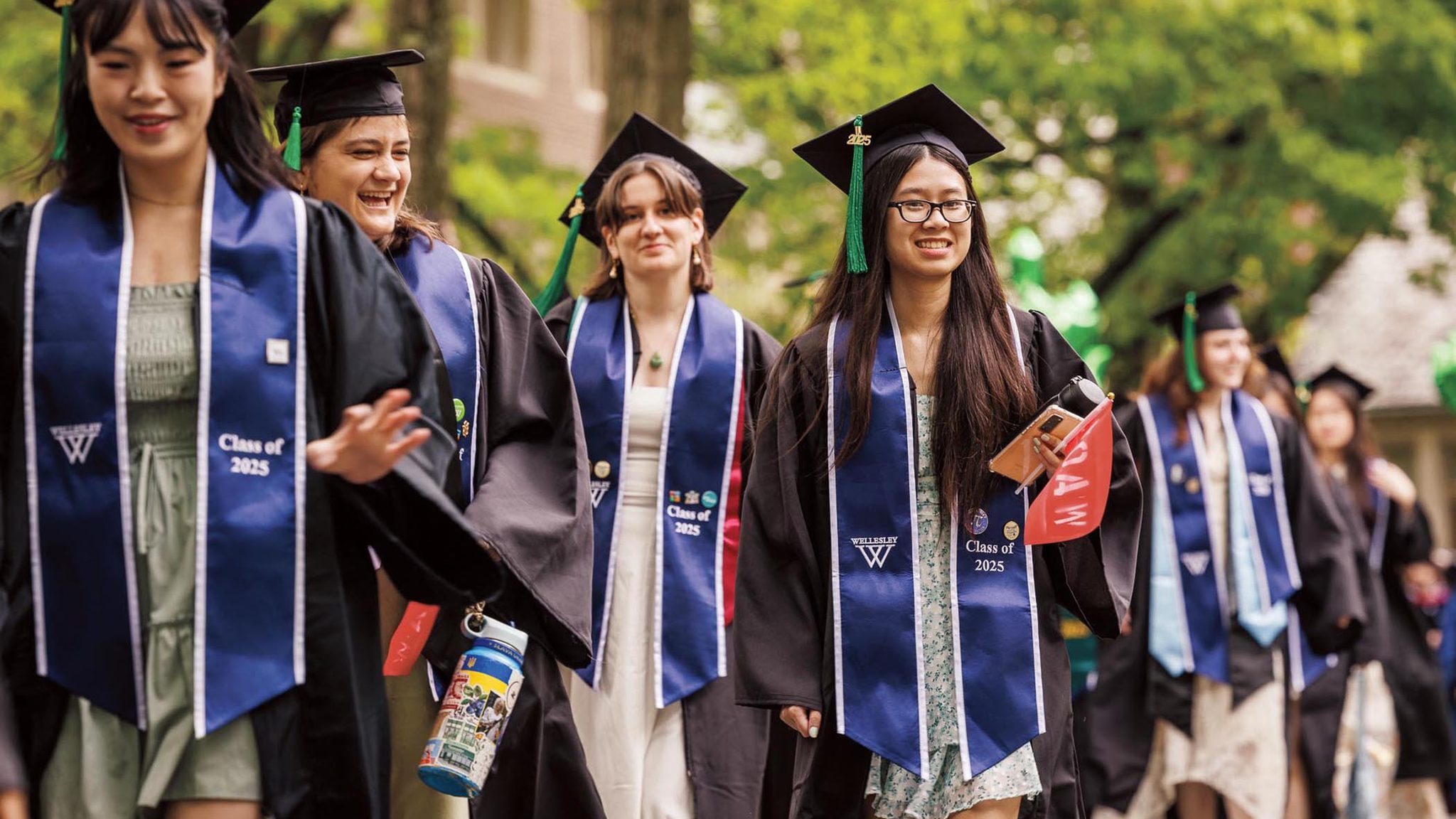 A line of students smiling and waving as they process in commencement