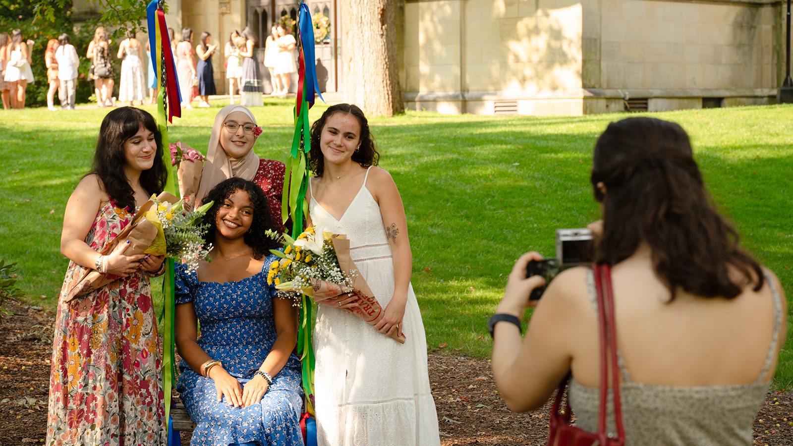 A small group of students poses for a photo at the swing. A line of students heading into the chapel is seen in the background.
