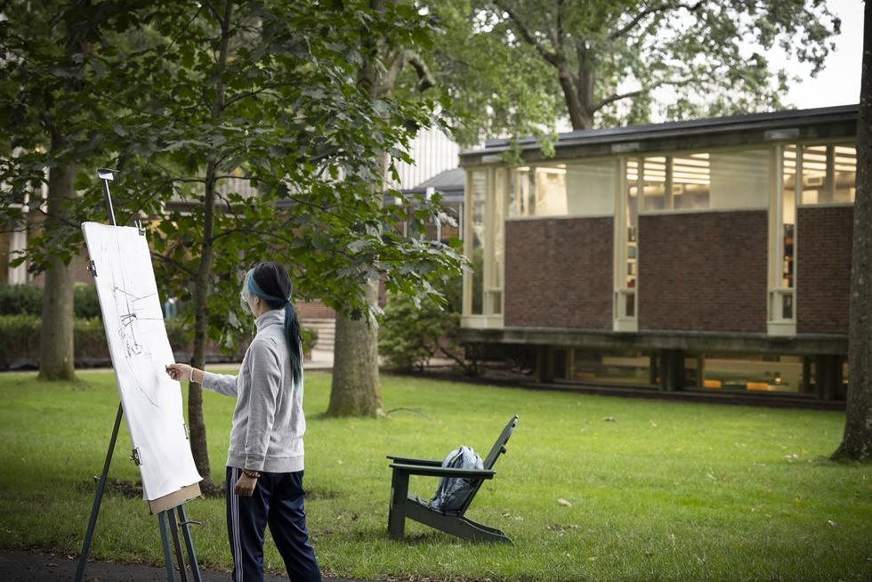 Student draws using an easel outside in the quad.