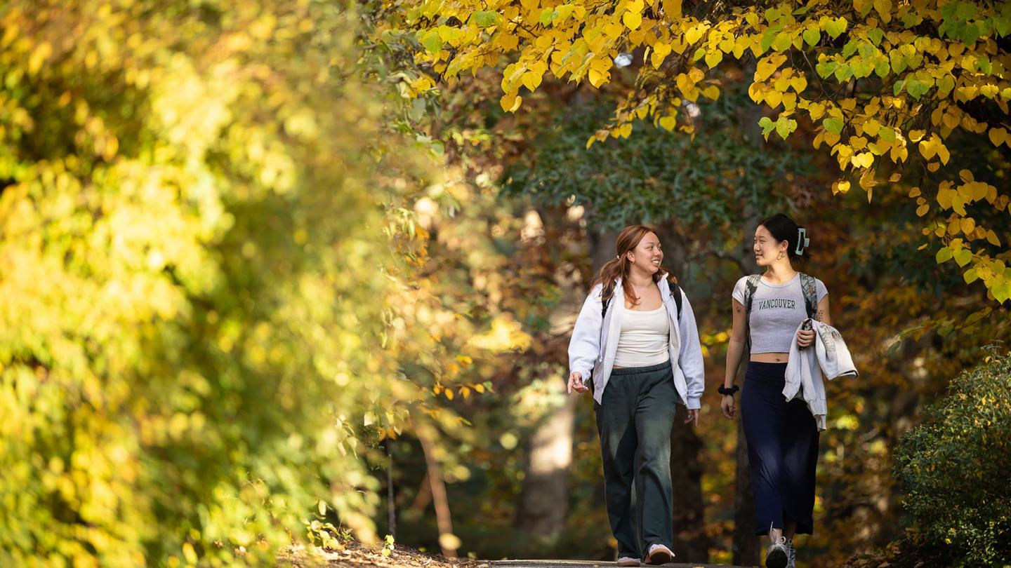 Two students walking and talking with fall foliage
