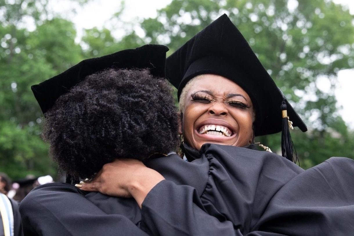 Two students hug on graduation day wearing their caps and gowns.
