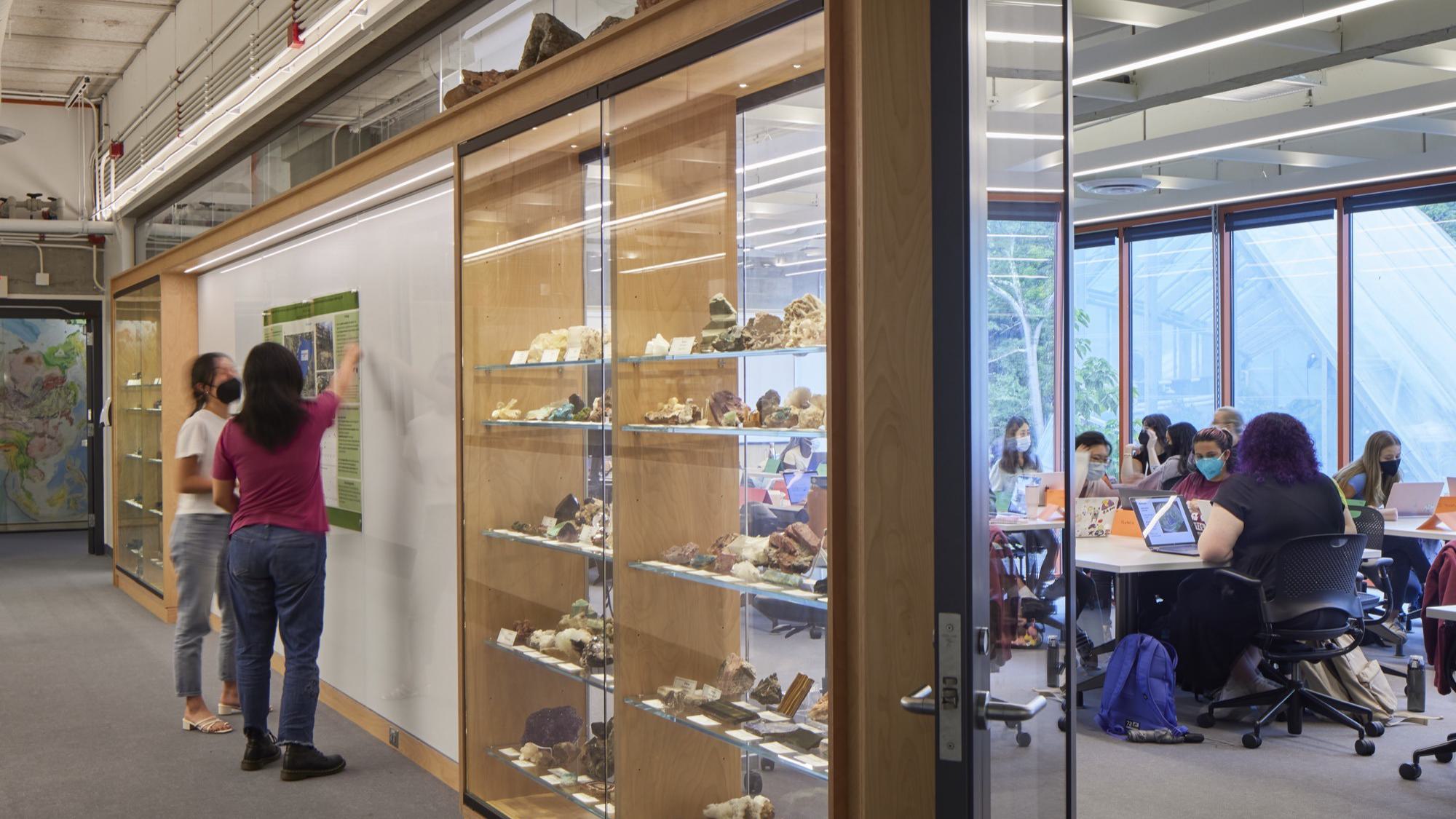 A classroom is seen beyond a glassed in wall of rocks on display