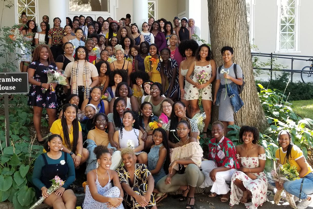 Large group of students of African descent pose in front of a white building.