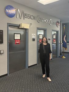 Molly Wasser stands in front of a wall that reads NASA Mission Control Center behind her